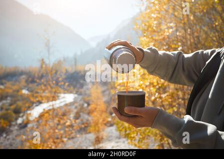 Femme touriste avec thermos et tasse avec café en automne lac camping dans les montagnes.Préparation du café concept extérieur Banque D'Images