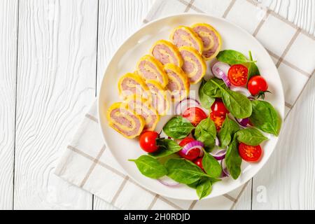 petits-déjeuners au jambon et au fromage hachés avec omelettes et salade d'oignons rouges aux épinards frais sur une assiette sur une table en bois blanc, vue horizontale depuis un Banque D'Images