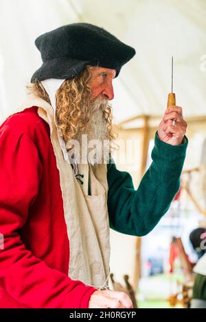 Reconstitution médiévale, vue latérale d'un homme âgé, avec une barbe complète, montre à une personne invisible, l'un de ses outils chirurgicaux debout. Banque D'Images
