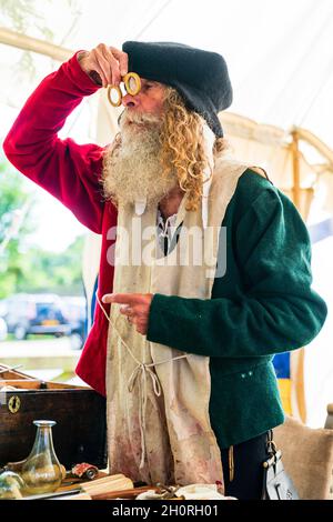 Reconstitution médiévale, vue latérale d'un homme âgé, avec une barbe complète, montre à une personne invisible, une paire de lunettes en les tenant au-dessus de son nez. Banque D'Images