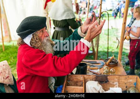 Reconstitution médiévale, vue latérale d'un homme âgé, avec une barbe complète, montre à une personne invisible, l'un de ses outils chirurgicaux assis à une table. Banque D'Images