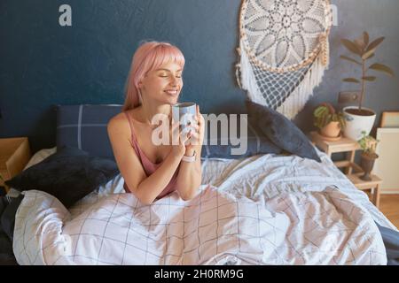 Belle dame tient une tasse assis sur un lit confortable le matin Banque D'Images