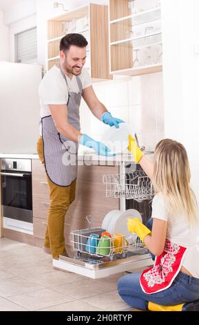 Jeune couple heureux de décharger lave-vaisselle avec de la vaisselle propre.Travailler ensemble et s'aider les uns les autres dans les travaux ménagers Banque D'Images