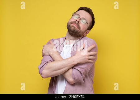 Mignon, barbu homme avec des lunettes se prend doucement et ferme les yeux de rêve.Arrière-plan jaune. Banque D'Images