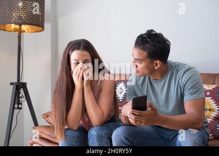Petit ami demandant des explications sur les messages cellulaires de téléphone tf sa petite amie assise sur un canapé dans le salon dans une maison avec un sombre Banque D'Images