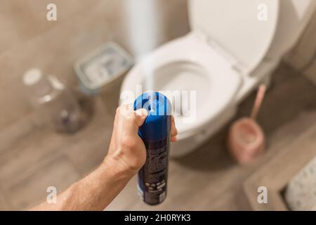 La main du gars tient et vaporise le désodorisant dans les toilettes ou la salle de bains.Concept d'hygiène à domicile. Banque D'Images