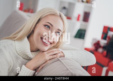 Photo portrait femme rêveuse souriante assise sur un canapé portant un chandail blanc tricoté Banque D'Images