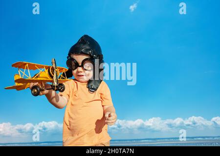 Un petit garçon dans un chapeau d'aviateur joue avec un jouet biplan Banque D'Images