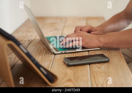 Gros plan des mains d'un homme tapant sur un clavier, à la recherche d'informations. Un rédacteur pigiste travaille sur un projet. Le concept de travail à distance. Photo de haute qualité Banque D'Images