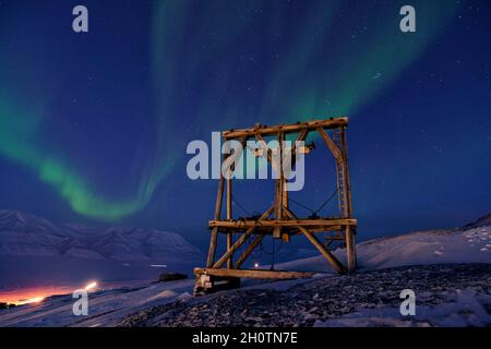 Saison sombre sur le Svalbard avec la nuit polaire et les lumières du nord. Pylône en bois de l'ancien tramway aérien pour transporter le charbon. Löhren, Spitsbergen Banque D'Images