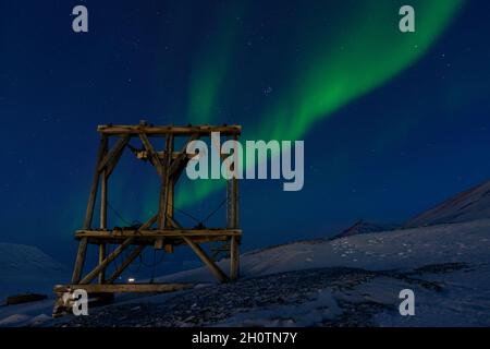 Saison sombre sur le Svalbard avec la nuit polaire et les lumières du nord. Pylône en bois de l'ancien tramway aérien pour transporter le charbon. Longyearbyen Norvège Banque D'Images