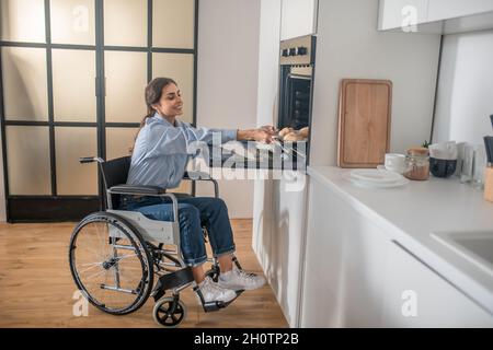 Une jeune fille sur un fauteuil roulant effectuant quelques travaux ménagers et regardant impliqué Banque D'Images