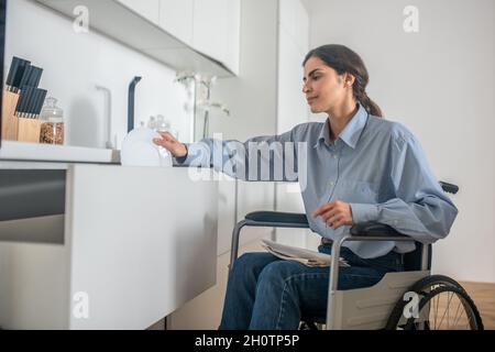 Une jeune fille sur un fauteuil roulant effectuant quelques travaux ménagers et regardant impliqué Banque D'Images