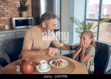 Famille prenant le petit déjeuner ensemble et papa essayant de nourrir son caghter Banque D'Images