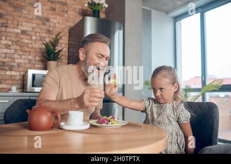 Famille prenant le petit déjeuner ensemble et papa essayant de nourrir son caghter Banque D'Images
