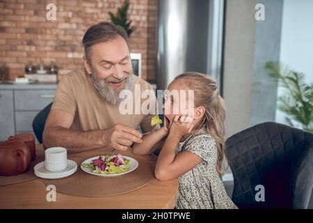 Famille prenant le petit déjeuner ensemble et papa essayant de nourrir son caghter Banque D'Images