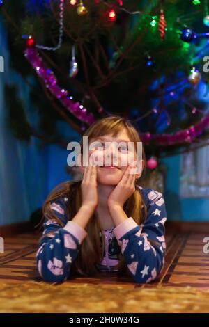 Defocus petite blonde caucasienne fille de 10 ans en pyjama se trouve près de l'arbre de Noël.Elle a mis sa tête dans ses mains.Le concept de sommeil, jour Banque D'Images