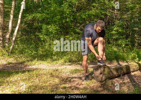 Le sportif enfile les lacets de ses jambes dans des baskets gros plan l'athlète court dans le parc à l'extérieur, autour de la forêt, les arbres de chêne vert herbe youn Banque D'Images