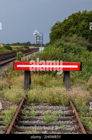 le vieux parement de chemin de fer désutilisé a surgrandi avec des mauvaises herbes avec des butées de tampon peintes en rouge et de vieux dortoirs en bois et des rails ou des voies rouillés. Banque D'Images