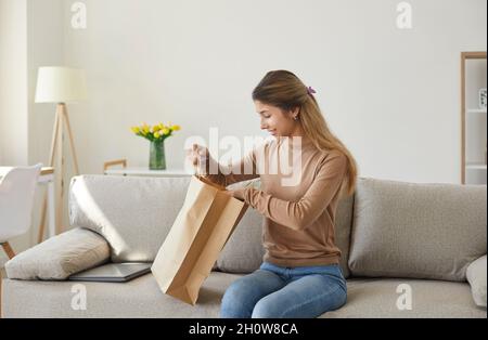 Une jeune femme satisfaite sort de son sac en papier sa commande longtemps attendue qu'elle a commandée sur Internet. Banque D'Images