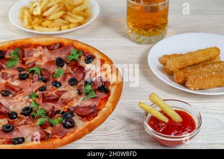 Pizza sur un plateau gros plan sur une table avec ketchup, jus, sauce et frites sur une table en bois blanc. Banque D'Images