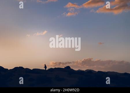 Silhouette d'un garçon marchant sur les rochers au coucher du soleil Banque D'Images