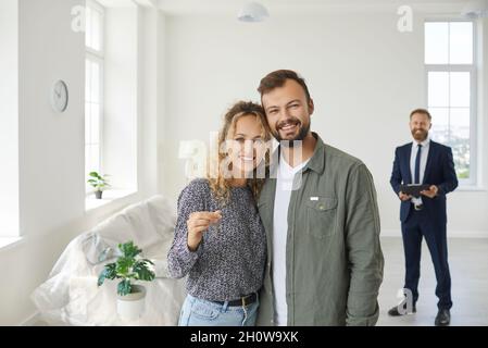 Un jeune couple heureux debout dans leur maison nouvellement achetée, souriant et montrant les clés Banque D'Images