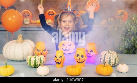 Une petite sorcière d'Halloween conjures des citrouilles avec une baguette magique.Un enfant heureux sourit et joue Halloween.Une fille espiègle vêtue d'une sorcière se produit Banque D'Images