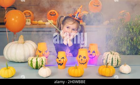 La petite sorcière fait des tours avec de la fumée colorée en utilisant une baguette magique.Un enfant heureux sourit et joue Halloween.Une fille gaie dans un cotu sorcière orange Banque D'Images