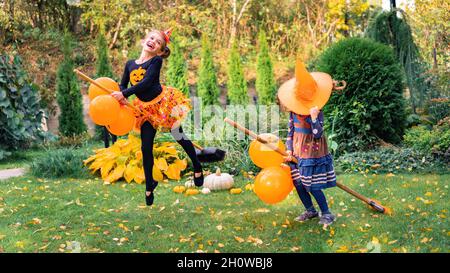 Une petite sorcière apprend à voler sur un bâton de poulet à la fête d'halloween.Les filles heureuses vêtues de sorcesses sautent sur un balai de rire.Les enfants sont des petits Banque D'Images