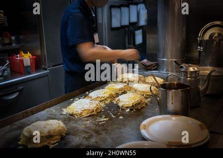 Un chef prépare un plat local très apprécié appelé okonomiyaki dans la cuisine d'Hiroshima, au Japon Banque D'Images