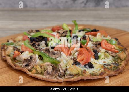 Pizza à croûte de chou-fleur fraîchement cuite avec garnitures de légumes hachées servie sur un plateau en bois. Banque D'Images