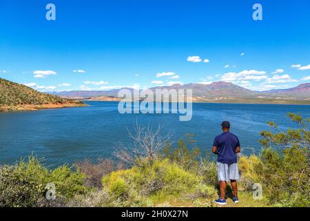 L'homme afro-américain par Roosevelt Lake dans le désert de l'Arizona.Homme noir contemplant le lac dans le désert de Sonoran en Arizona, par un ciel bleu ensoleillé. Banque D'Images