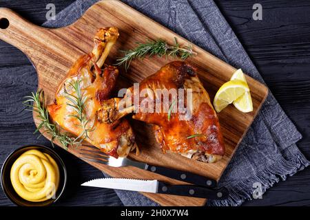 tiges de porc grillées croustillantes sur une planche en bois avec couverts, romarin, quartiers de citron et moutarde, vue horizontale depuis le dessus, plat Banque D'Images