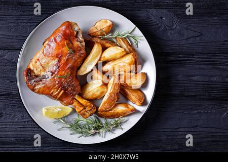tiges de porc grillées croustillantes sur une assiette avec des quartiers de pommes de terre, du romarin, du citron sur une table en bois noir, vue horizontale depuis le dessus, plat, espace libre Banque D'Images