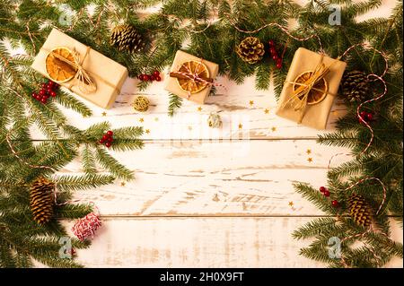 Arrière-plan de Noël blanc en bois avec branches et cônes d'épicéa, cadeaux en papier kraft, avec tranche d'orange, cannelle, anis. Vue du dessus Banque D'Images