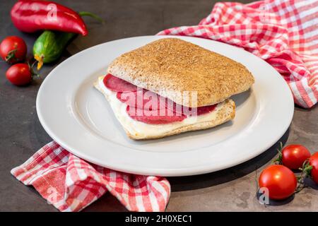 Sandwich au salami et au cheddar sur une assiette en porcelaine blanche sur une table en pierre Banque D'Images