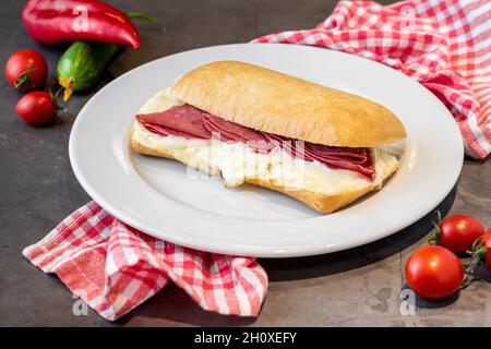 Sandwich au salami et au cheddar sur une assiette en porcelaine blanche sur une table en pierre Banque D'Images