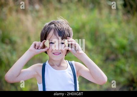 Enfant d'âge préscolaire doux, garçon, tenant des biscuits devant ses yeux, souriant, fond de la nature lui incommode Banque D'Images