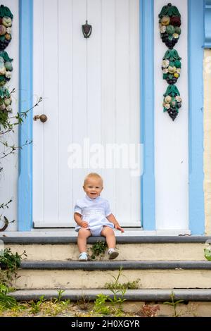 Beau petit garçon, assis sur le porche avant dans les rues de Clovelly, joli vieux village au coeur du Devonshire, Angleterre Banque D'Images