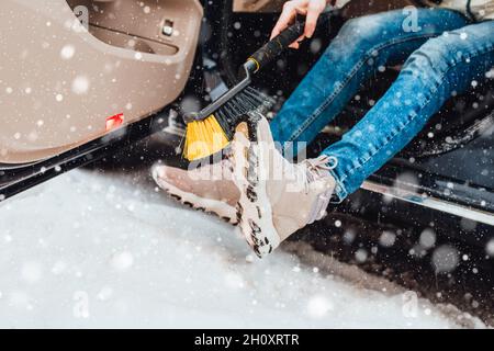 Femme en hiver dans la neige lourde brosse les chaussures de la neige avant d'entrer dans la voiture - entretien de voiture Banque D'Images