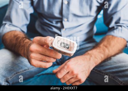 Mesure du niveau d'oxygène et de la fréquence de pouls à l'aide d'un oxymètre de pouls portable - un homme surveille sa santé - saturation 95 pouls 84 Banque D'Images