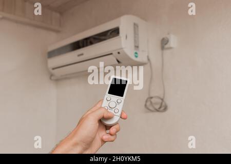 La main du gars tient la télécommande du climatiseur.Refroidissement et contrôle de la température dans la pièce de la maison. Banque D'Images