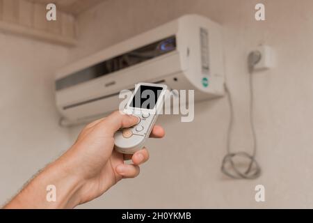 La main du gars tient la télécommande du climatiseur.Refroidissement et contrôle de la température dans la pièce de la maison. Banque D'Images