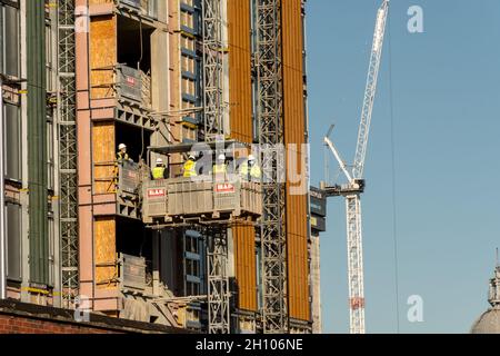 Gros plan des travailleurs d'un ascenseur portant un équipement de sécurité sur le chantier de construction d'un grand bâtiment avec une grue à tour en arrière-plan. Banque D'Images