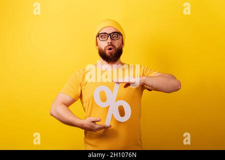 un homme choqué tient 3d signe de pourcentage sur fond jaune, des réductions avec un intérêt élevé Banque D'Images