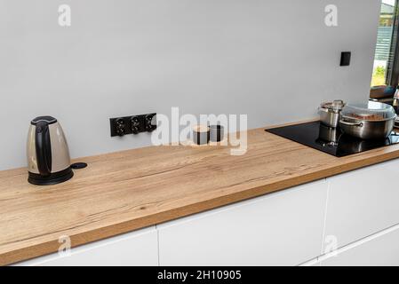 Une bouilloire électrique située sur le plan de travail des armoires de cuisine, un bol à sucre et un réservoir de lait visibles. Banque D'Images