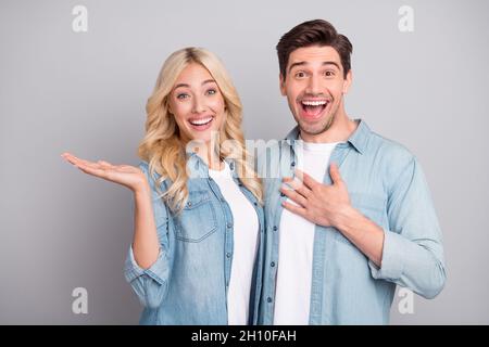 Photo de jeune couple heureux positif sourire tenir main produit offre annonces vente suggérer isolé sur fond gris couleur Banque D'Images