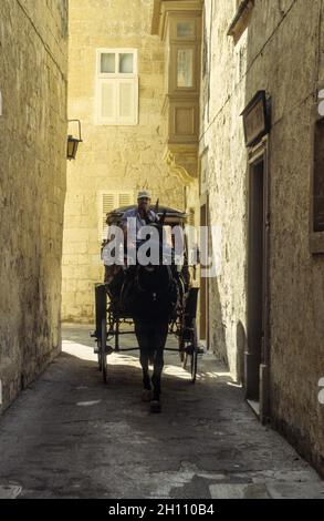 Un taxi avec des touristes dans les ruelles étroites de la vieille ville de Mdina sur l'île de Malte. Banque D'Images