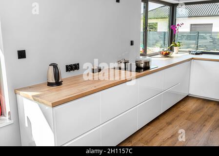 Pots métalliques sur une cuisinière à induction intégrée au plan de travail de la cuisine, sur les armoires, une bouilloire électrique est visible. Banque D'Images